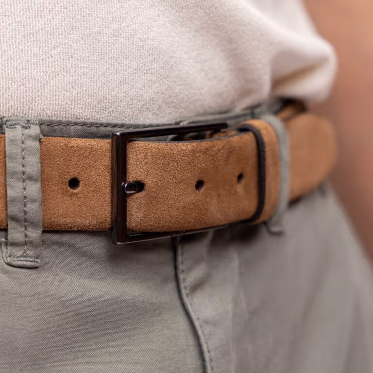 Close-up of a brown suede belt with a black buckle worn with light gray pants and a white shirt.