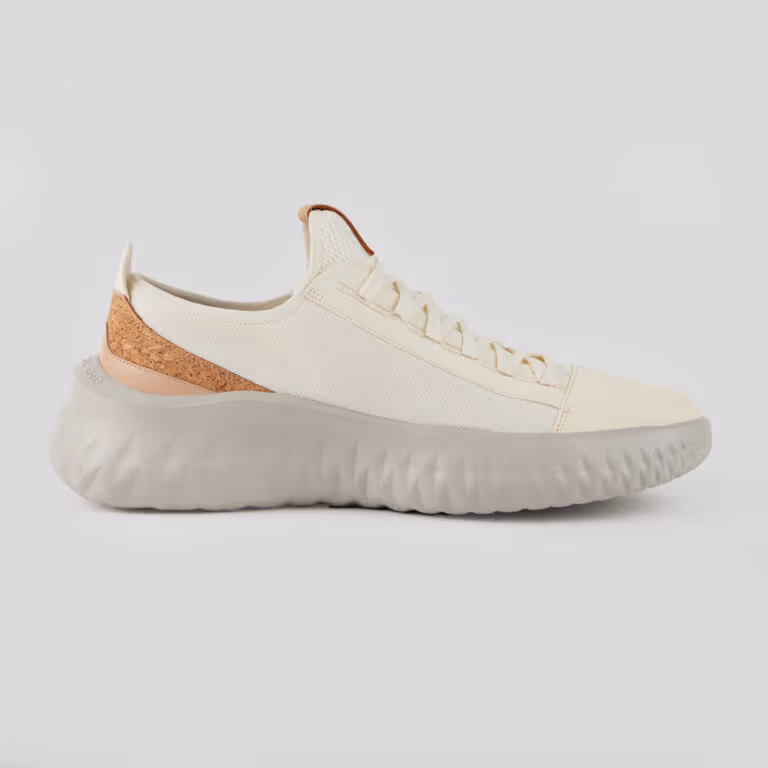 Side view of a cream-colored sneaker with a textured light gray sole and cork detailing on the heel.