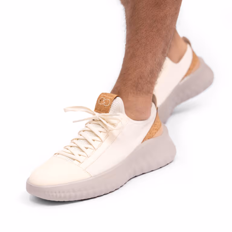 Leg wearing a white sneaker with cork accents and a light gray sole on a white background.