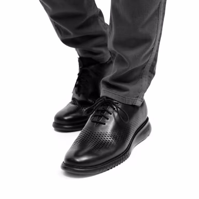 Person wearing black perforated leather dress shoes and gray pants.