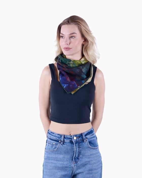 Woman with blonde hair wearing a black sleeveless crop top, blue jeans, and a colorful scarf tied around her neck, looking to the side.