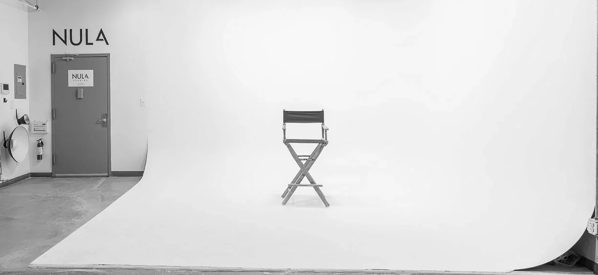 An empty studio cyclorama with a single director’s chair on the white sweep