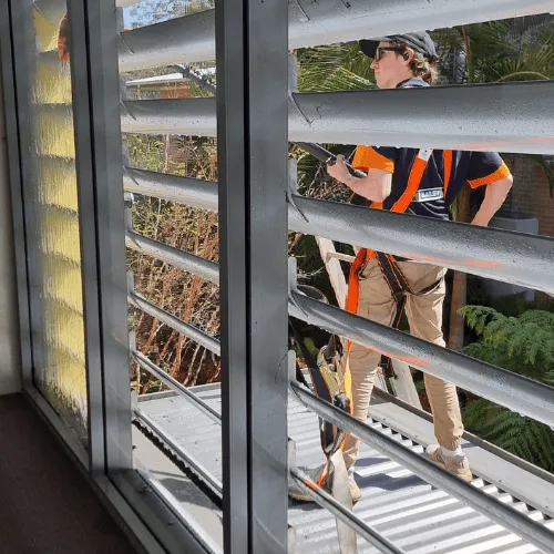 Window cleaner in a safety harness cleaning external louvre windows