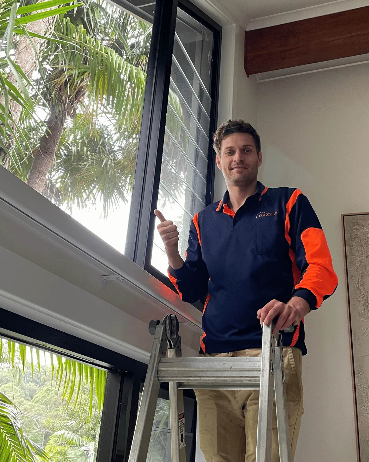 Dazzler team member on a ladder cleaning high windows