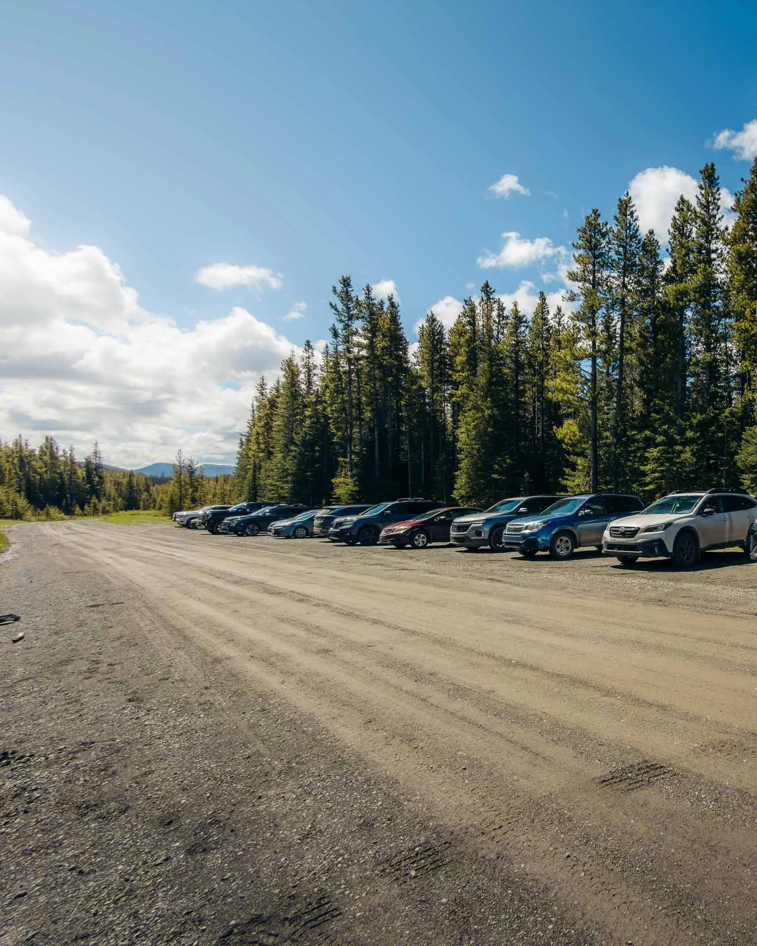 Cars parked along the gravel Powderface Trail road at the Jumpingpound Summit Trailhead in Kananaskis.