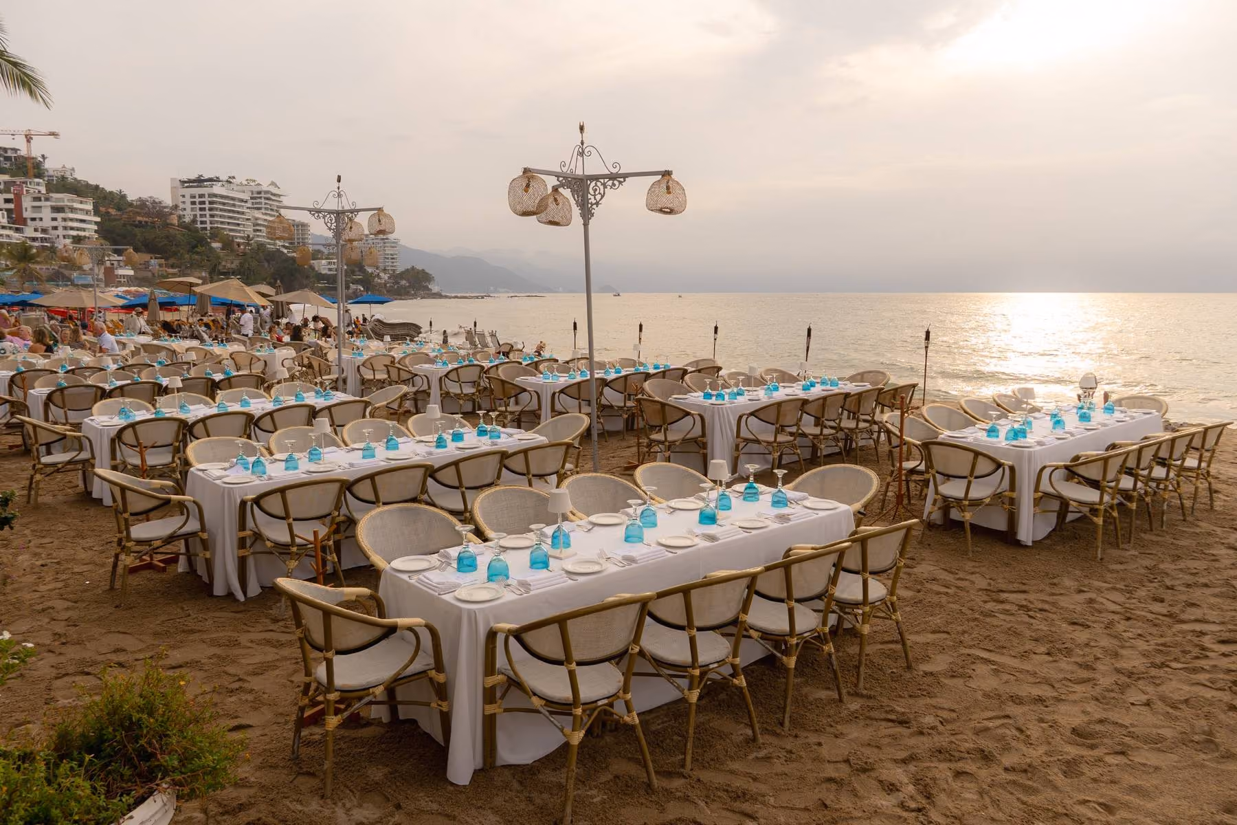 Long tables set for a group dinner on the sand at El Dorado, facing the sea at golden hour