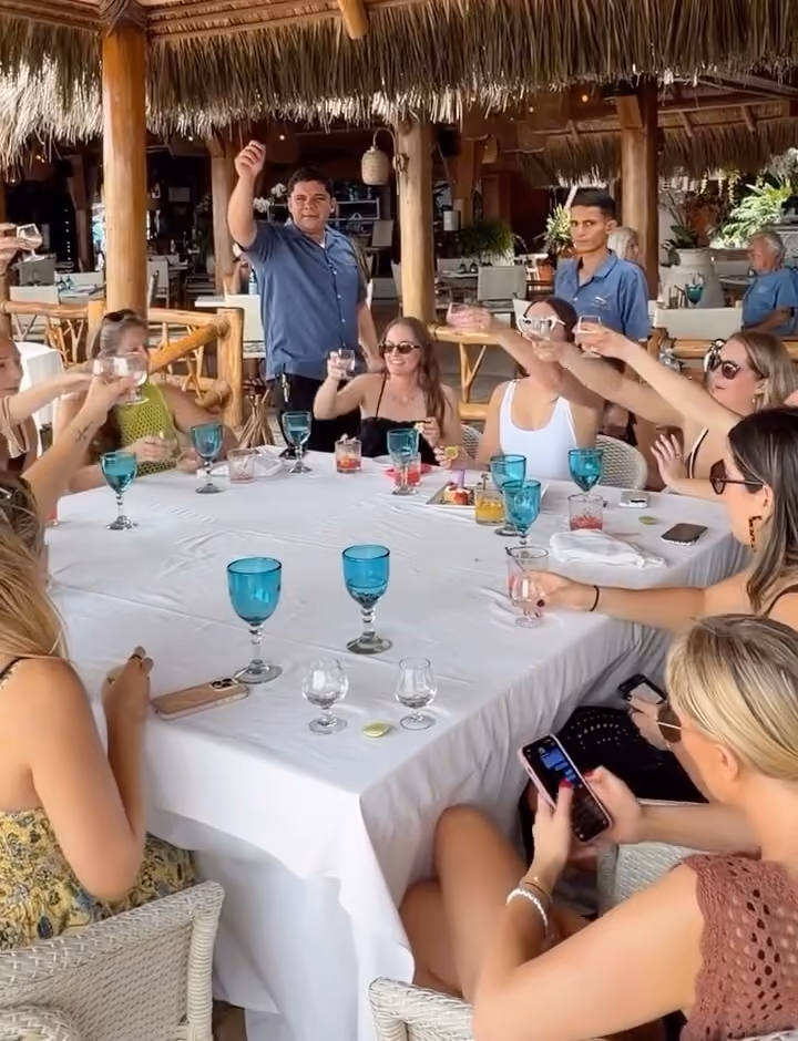 Bachelorette group raising a toast at a long table under the El Dorado palapa
