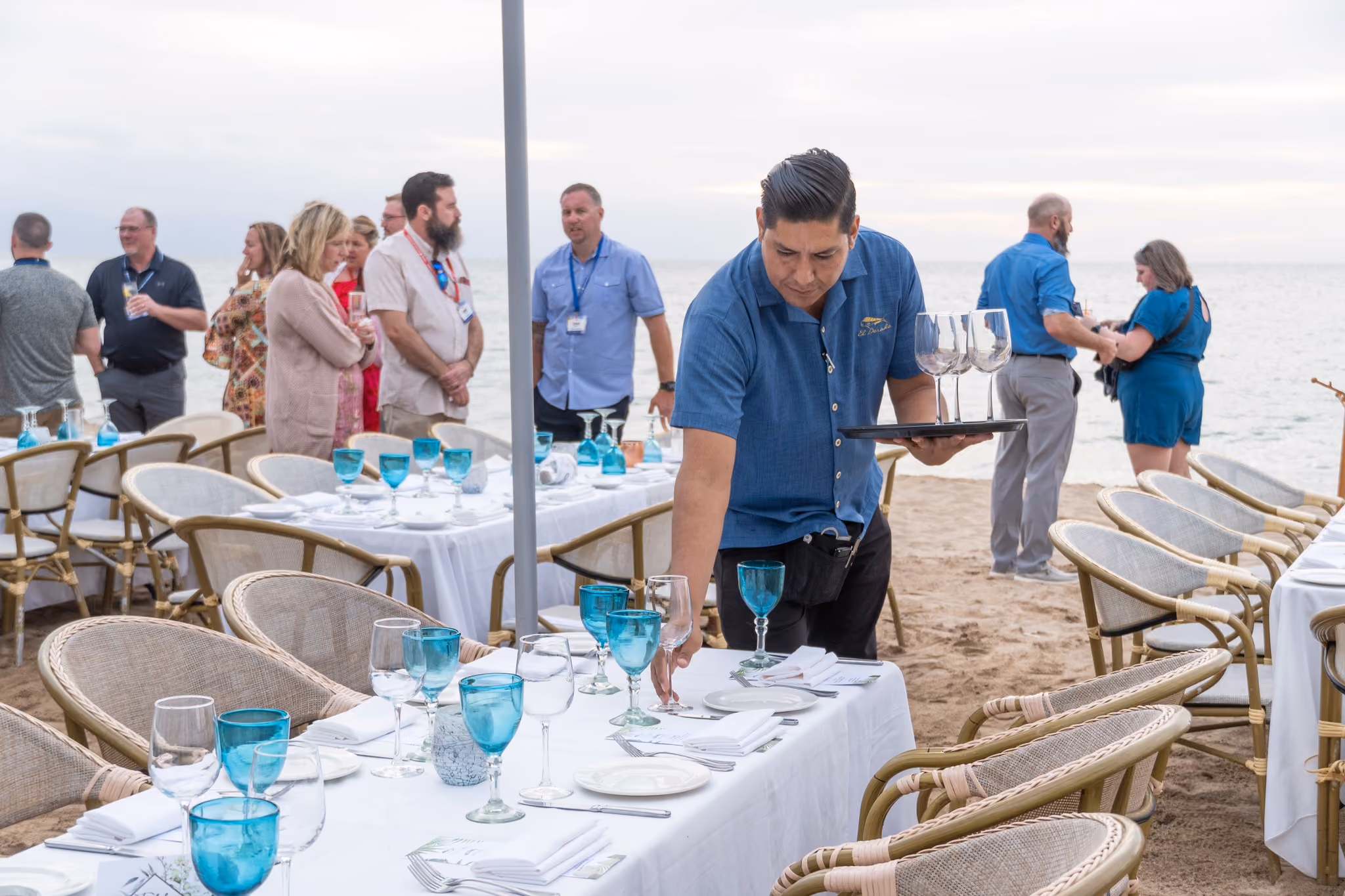 Corporate group gathering on the beach while a server sets long tables for dinner at El Dorado