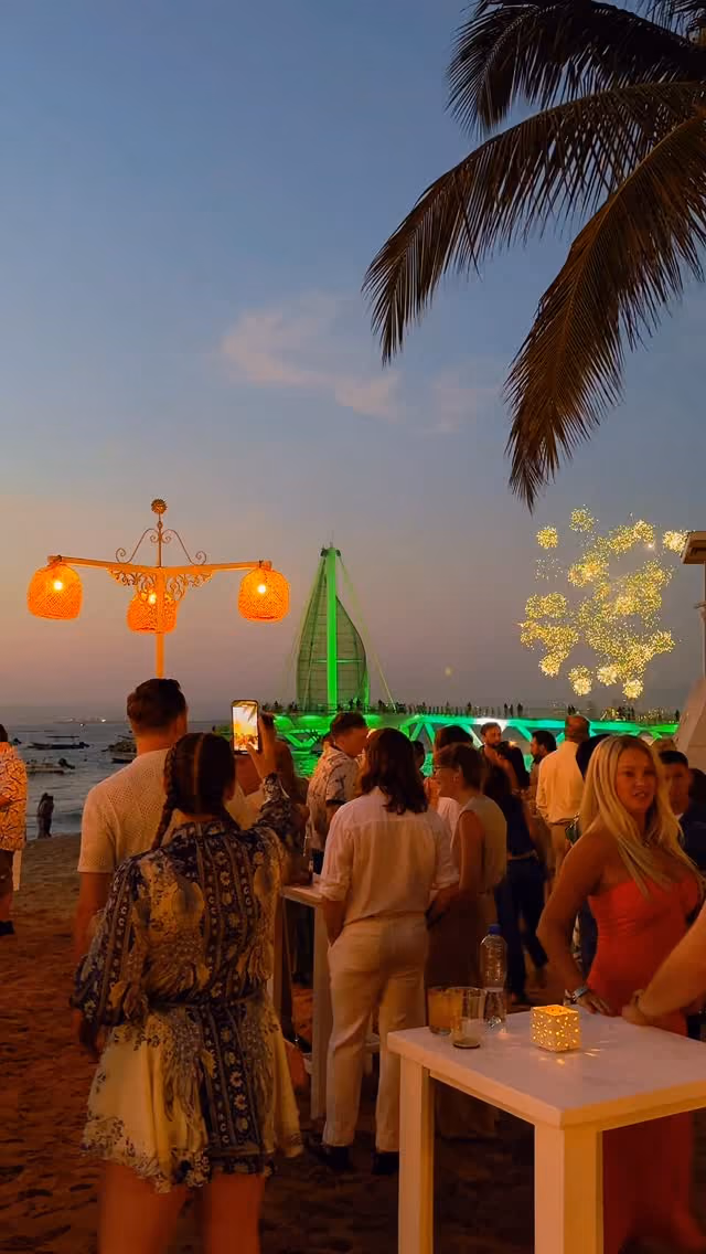 Guests at a welcome party on the beach at sunset, with the Los Muertos pier lit up behind