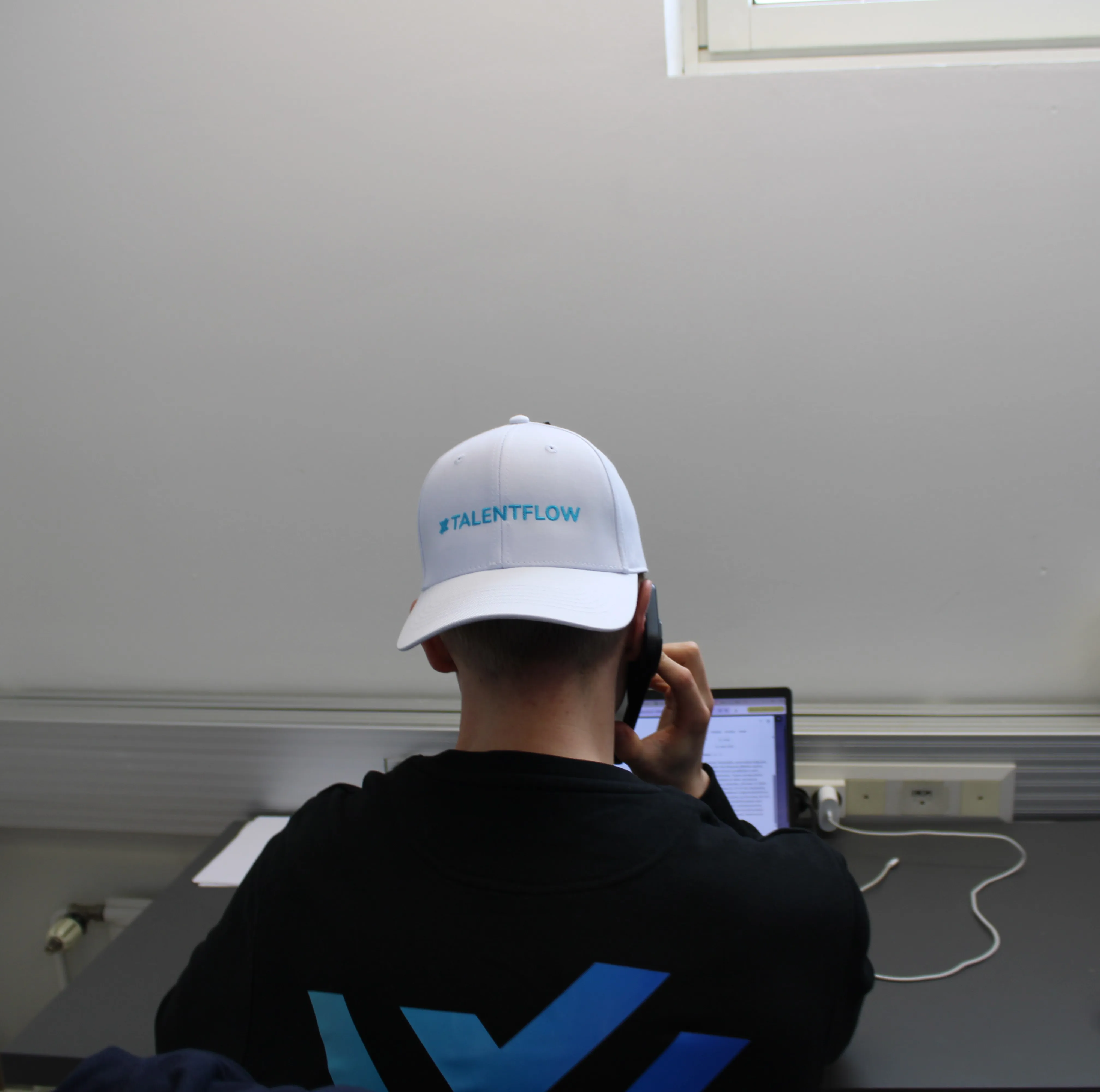TalentFlow-lippalakkipainen työntekijä puhuu puhelimessa työpöydän ääressä