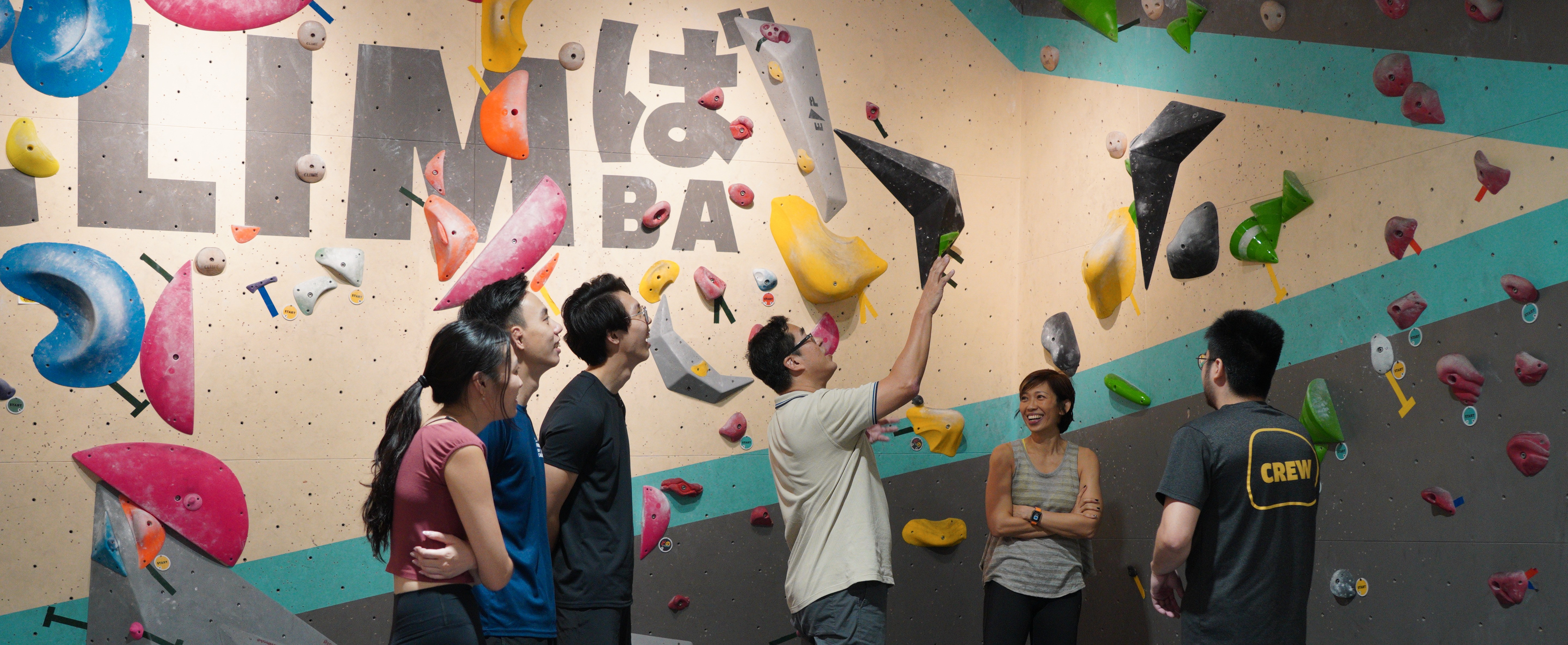 A first-time climber mid-route on Climba's bouldering wall, coach spotting from below