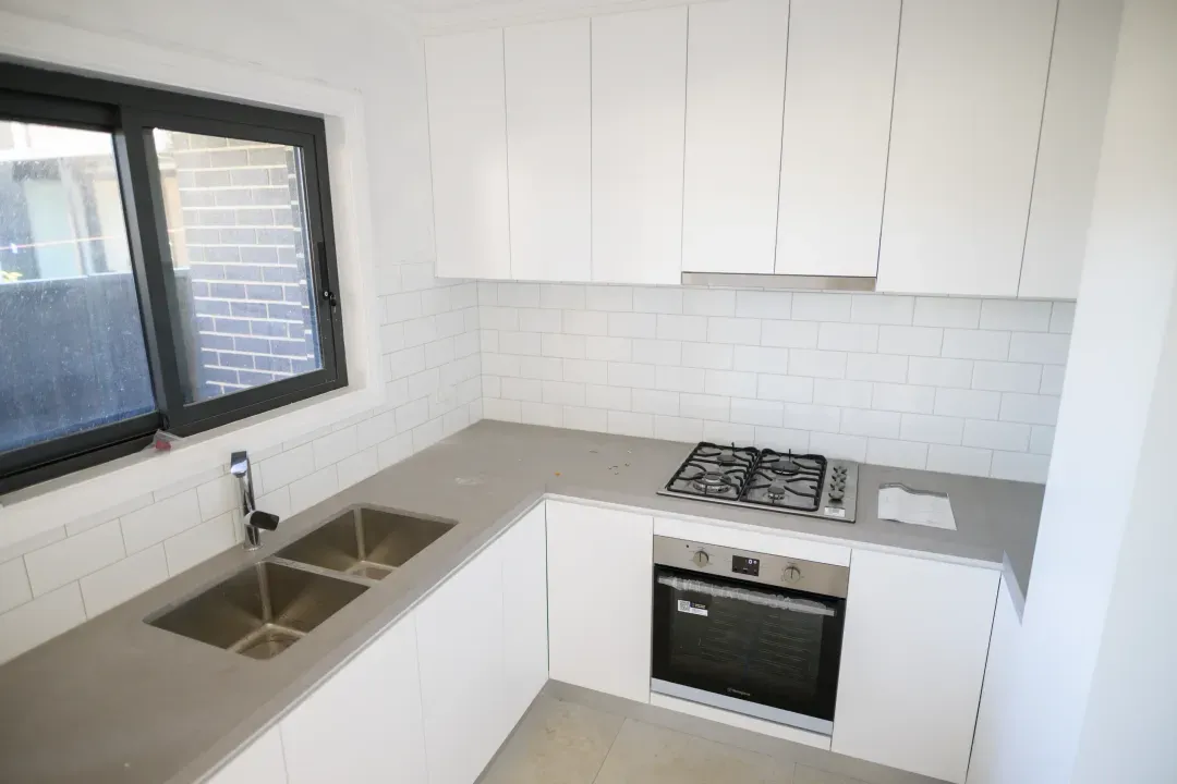 Granny flat kitchen with white cabinets, stone benchtop and gas cooktop