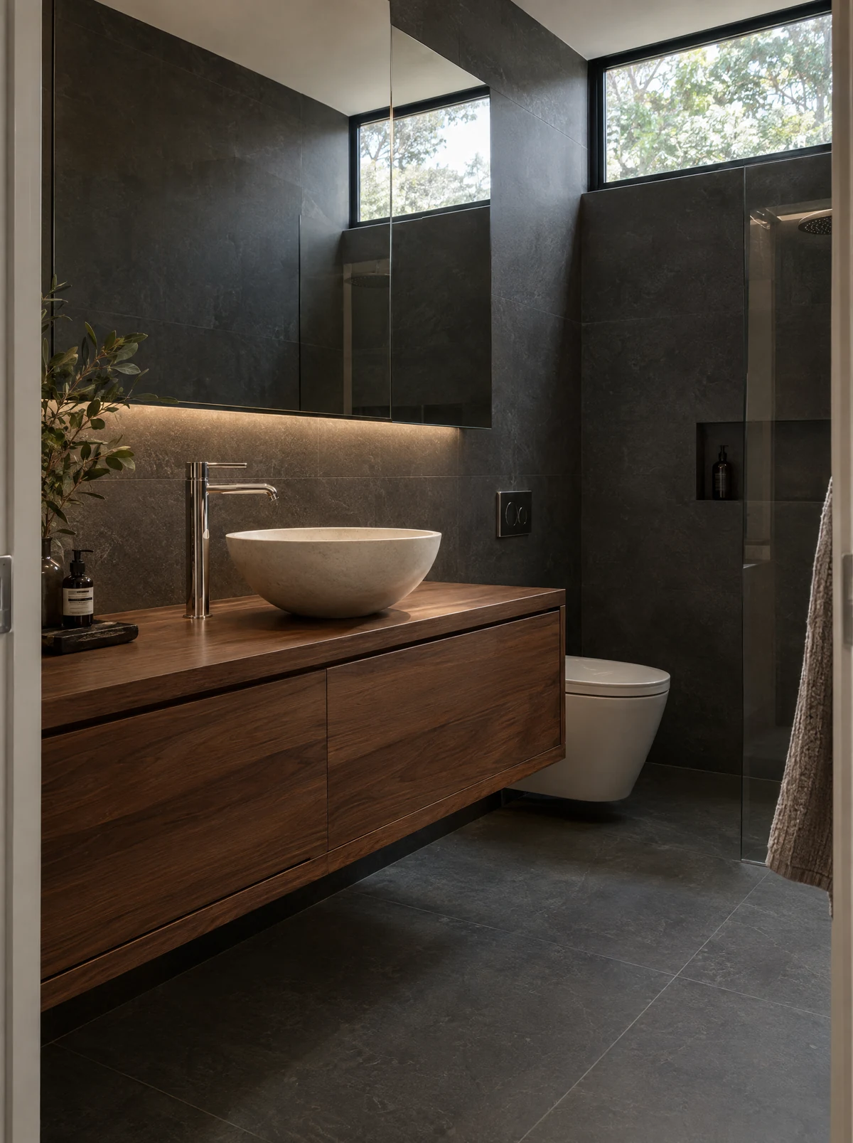 Dark bathroom combining walnut joinery and basalt surfaces