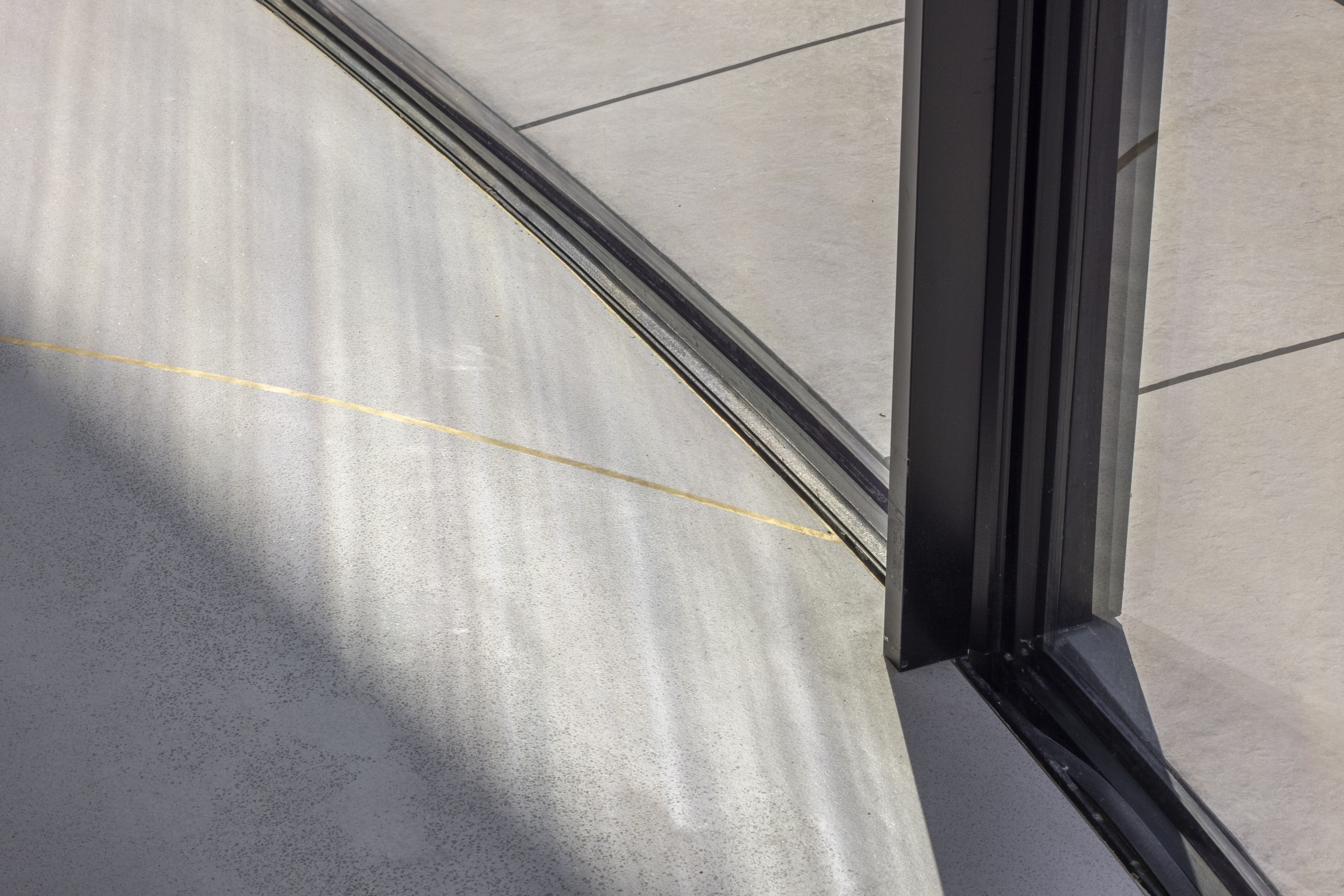 Détail d’un profilé aluminium noir à la jonction de deux vitrages, sur un sol en béton ciré