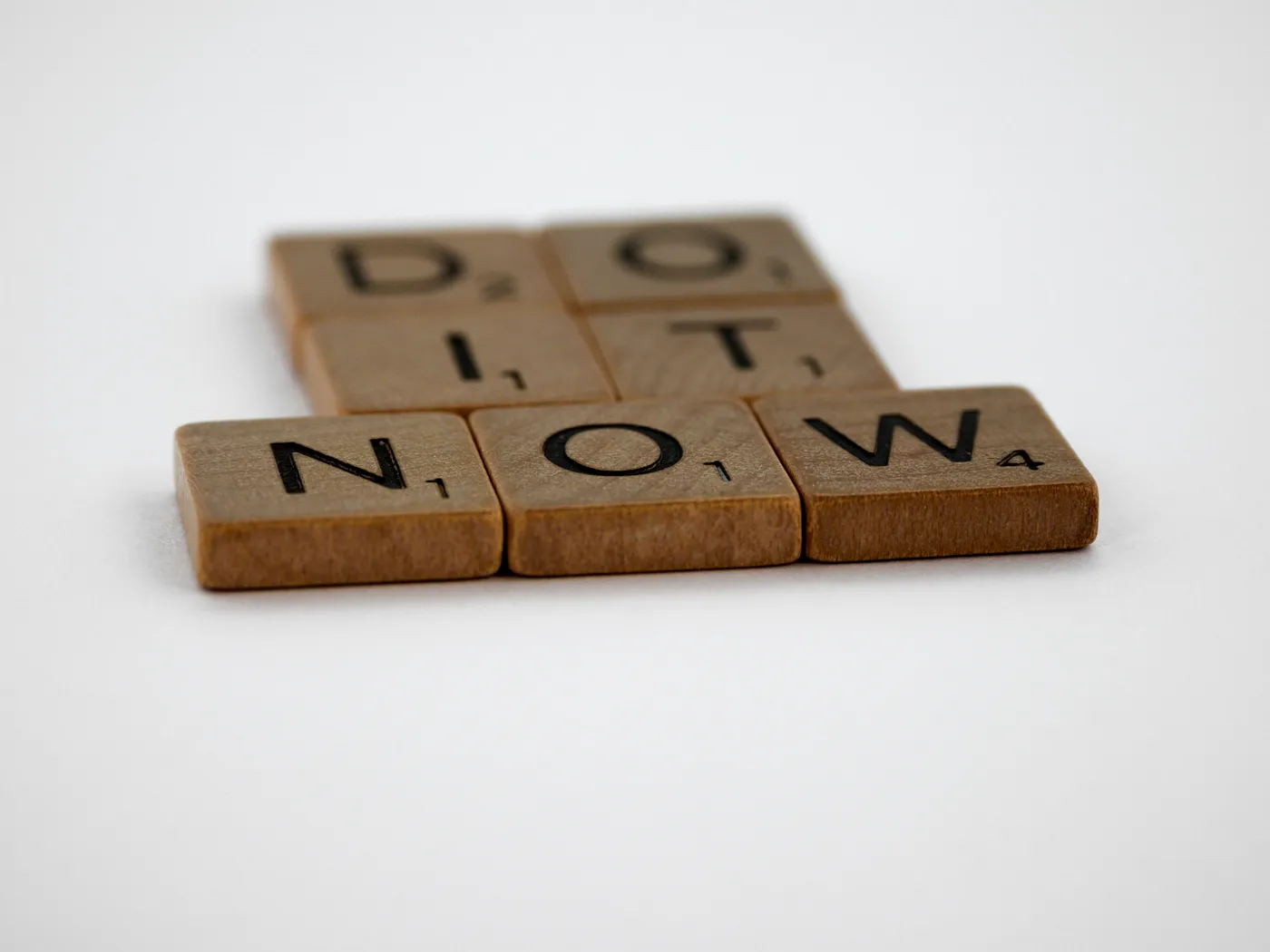 Wooden blocks on a white background spell out 'DO IT NOW', emphasizing the message of taking immediate action and the urgency of productivity.