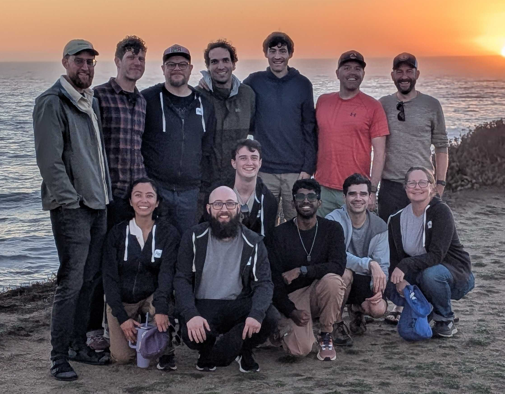 13 ReSim team members pose in front of a sunset after a team hike along the coast in California