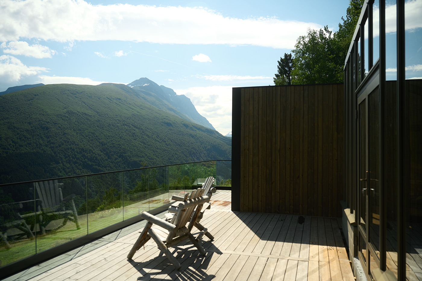 To stoler står på en terrasse med utsikt over norsk natur. Hytte i bakgrunnen