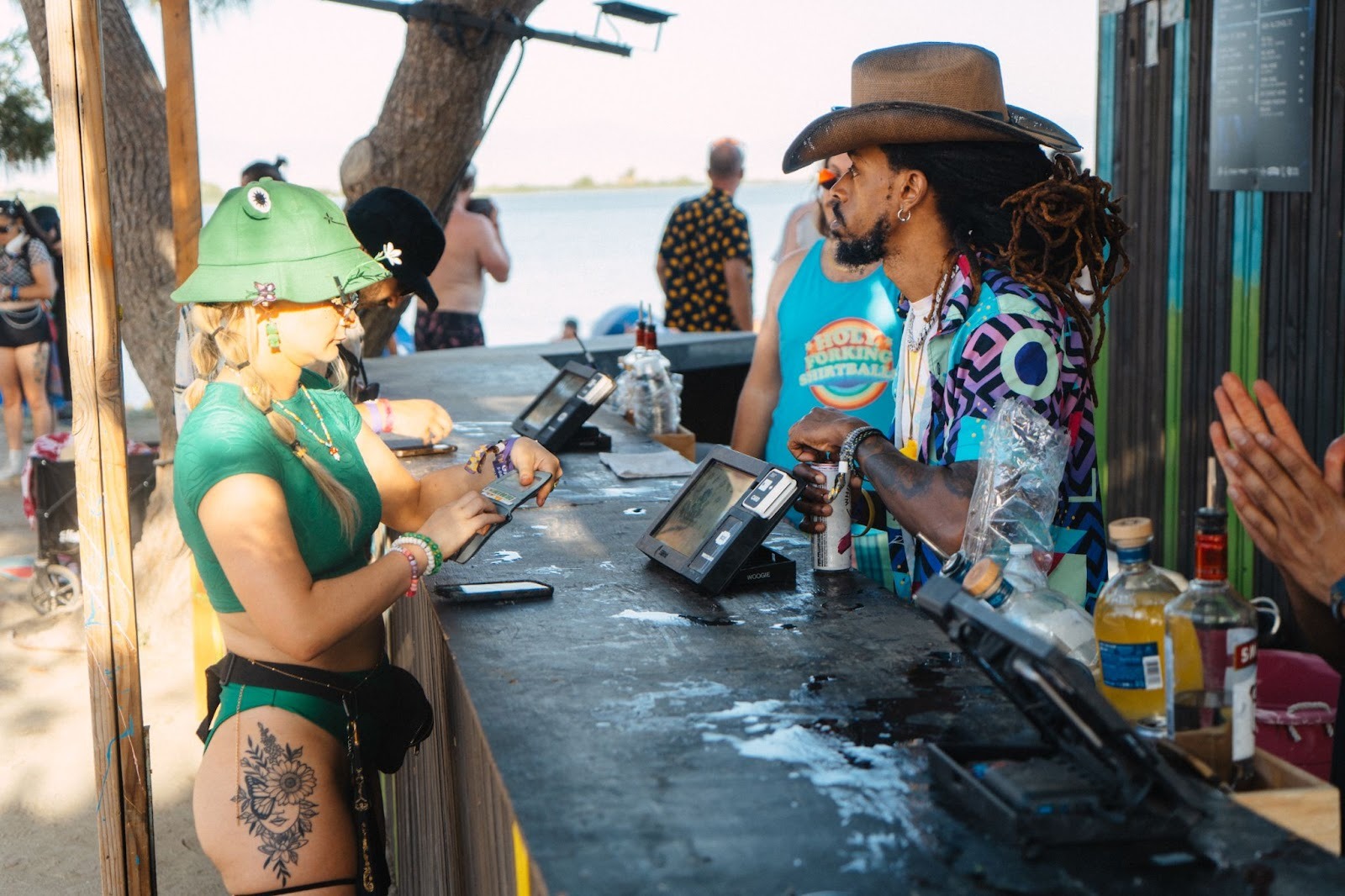 Attendee paying at a waterfront festival bar using a contactless card reader while the bartender assists