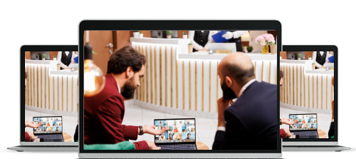 Two men in suits sitting and video conferencing on a laptop in a modern office or lobby setting.