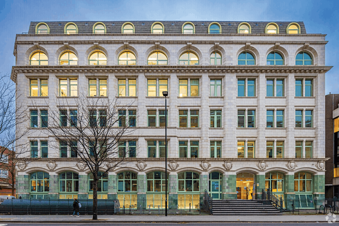 Multi-storey classical office building with arched windows and a tree in front on a city street.