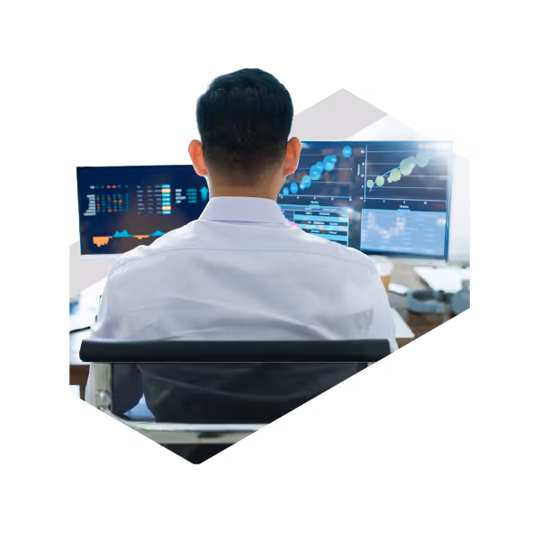 Financial analyst working at dual monitor trading desk displaying stock market charts and data analytics