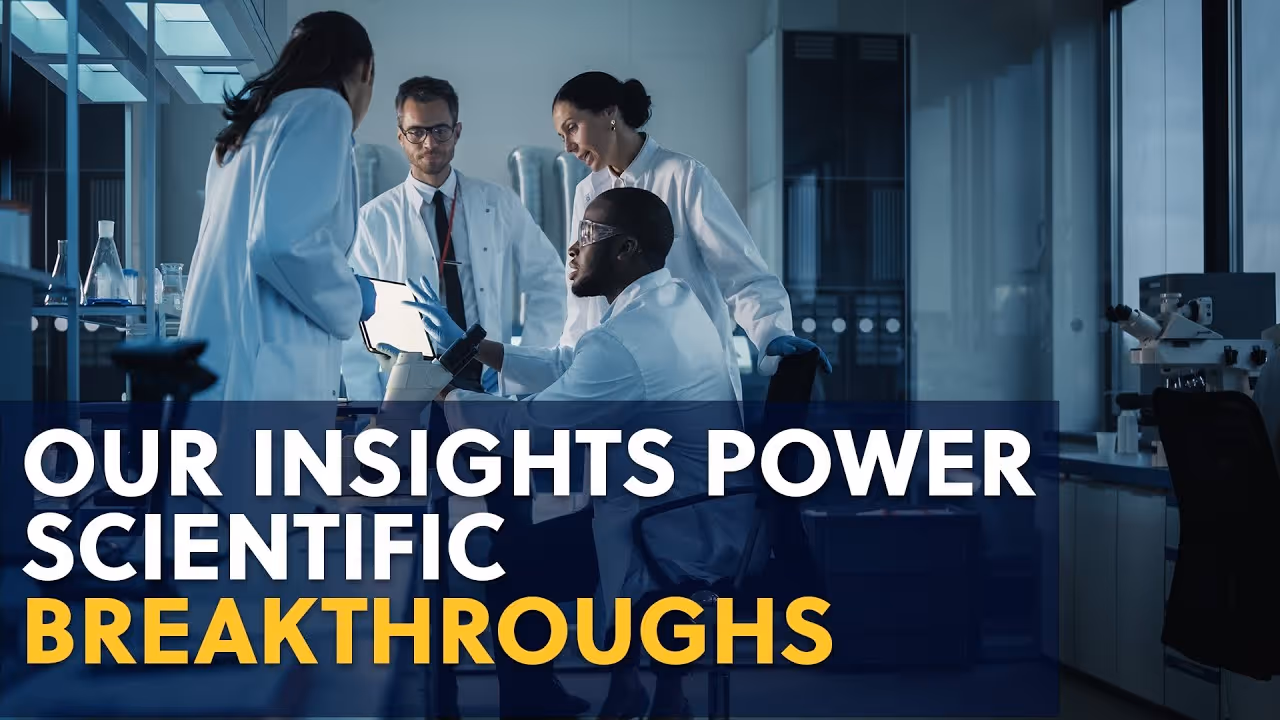 Four scientists in lab coats discuss data on a tablet in a laboratory setting.