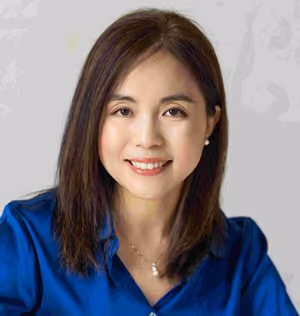 Portrait of a smiling woman with straight brown hair wearing a blue blouse and pearl earrings.