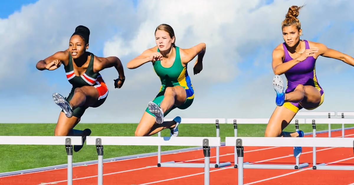 Three women jumping over hurdles on a track during a race.
