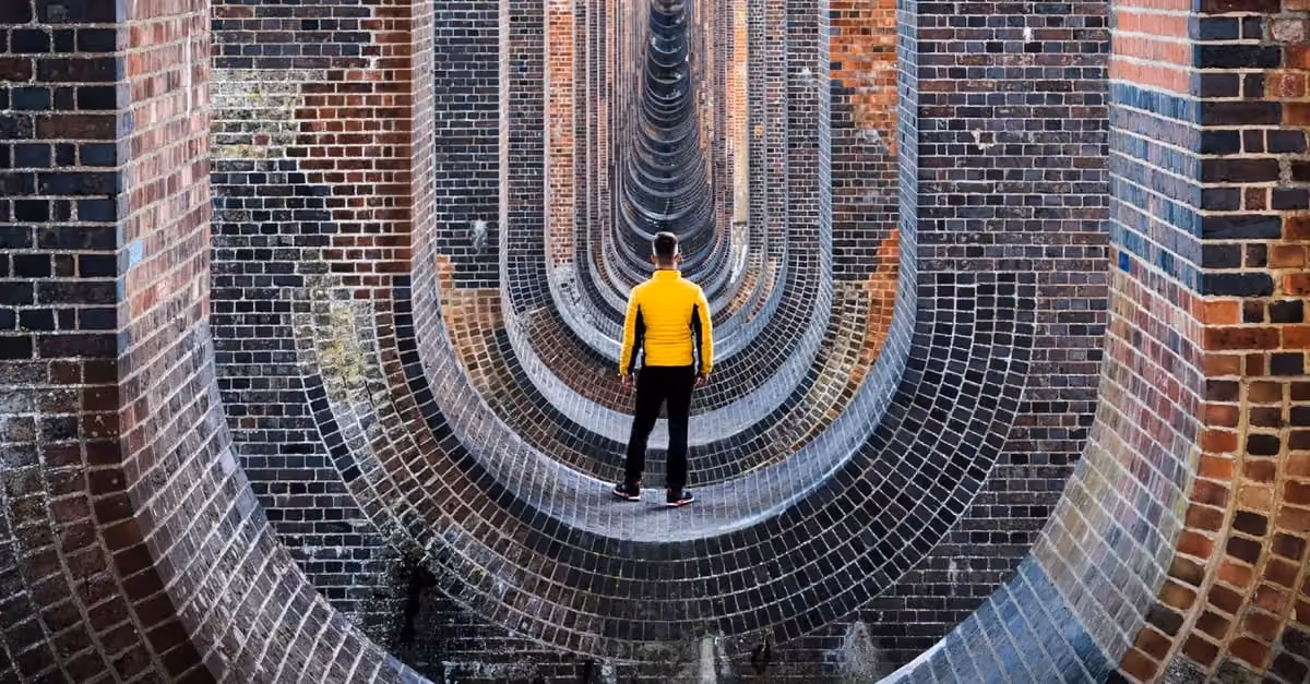 A person in a yellow jacket stands in a brick railway arch tunnel creating a symmetrical perspective.