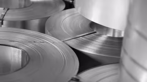 Rolls of industrial sheet material stacked in a factory, shown in monochrome.