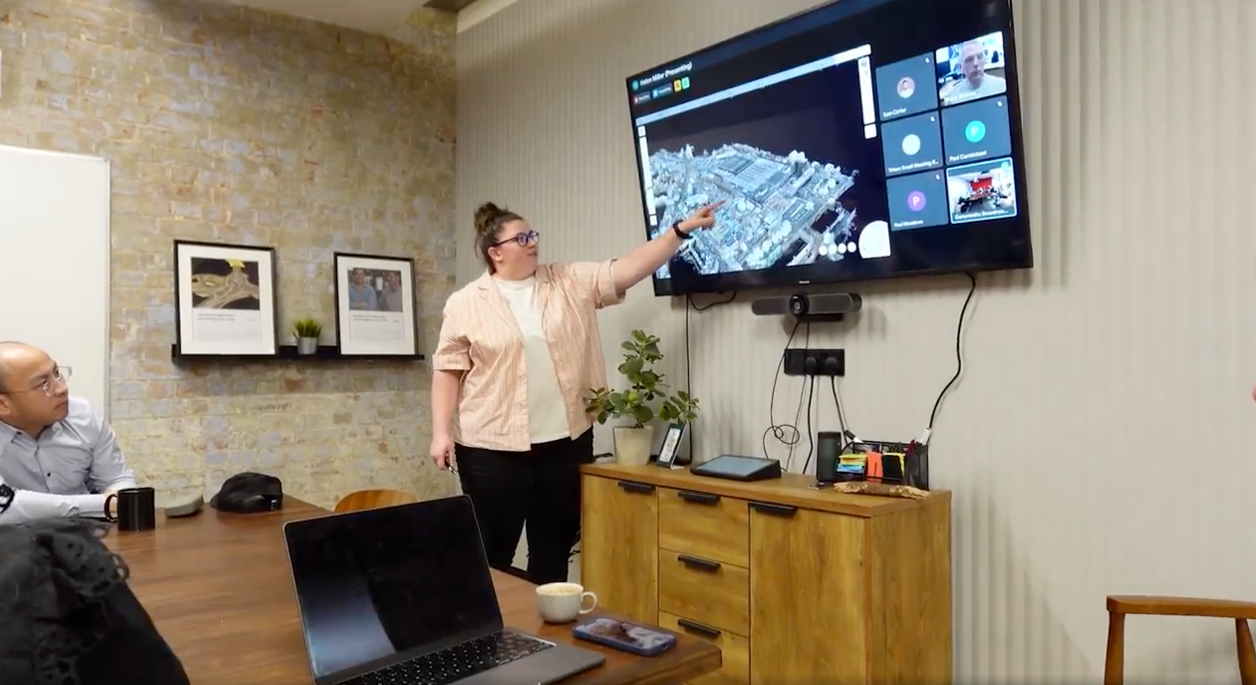 Team member pointing at a view in Sensat on a screen during a hybrid meeting, with remote colleagues joining by video call.