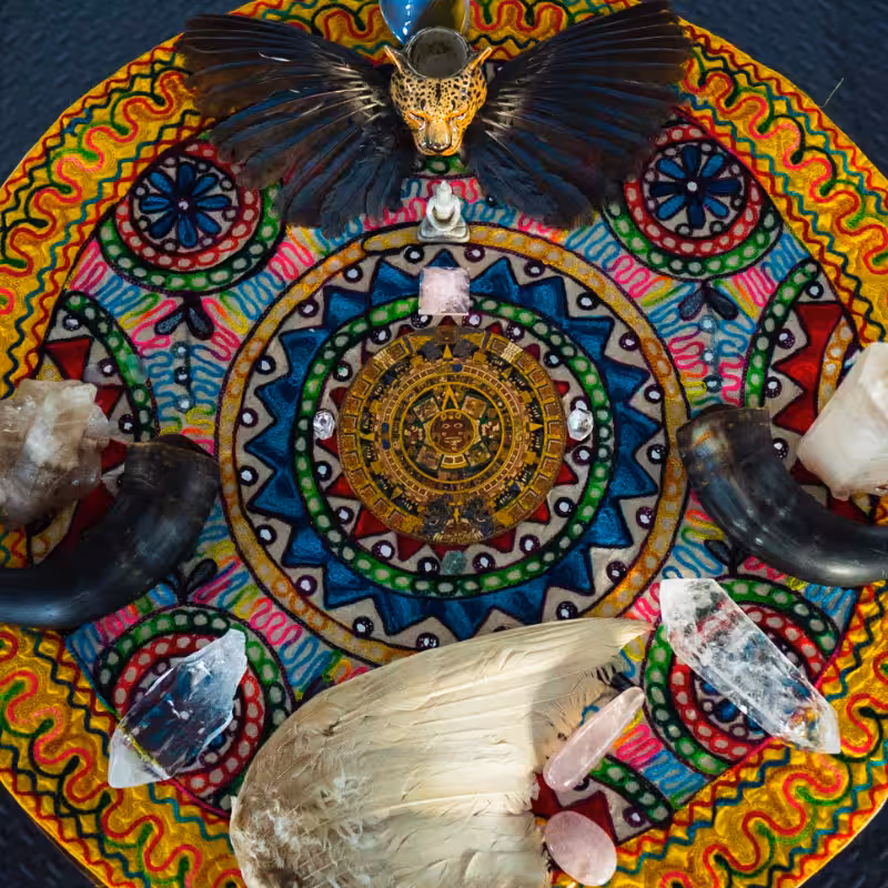 A vibrant spiritual altar featuring crystals, feathers, animal horns, and a colorful mandala centerpiece.