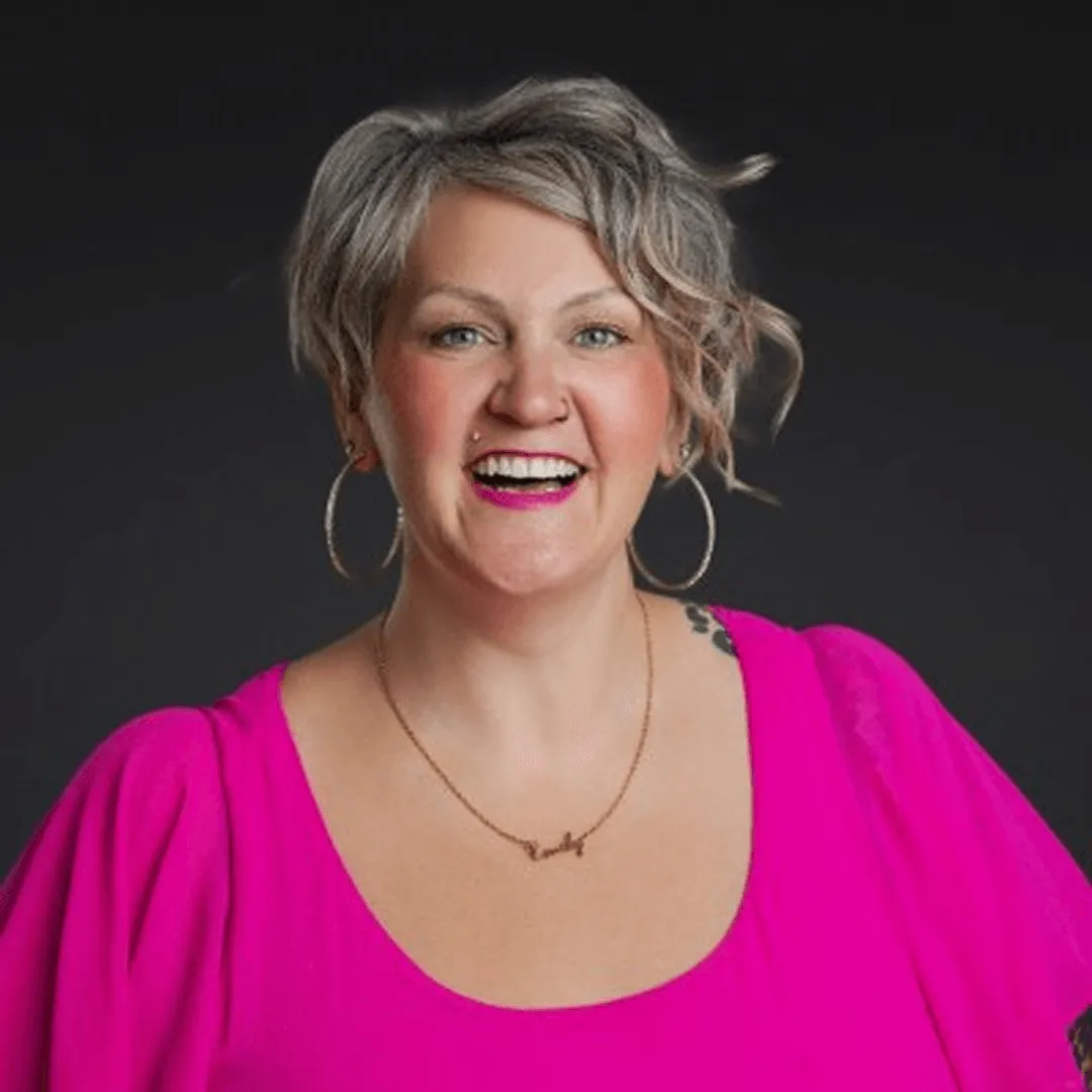 Woman smiling in a bright pink top with short wavy hair.