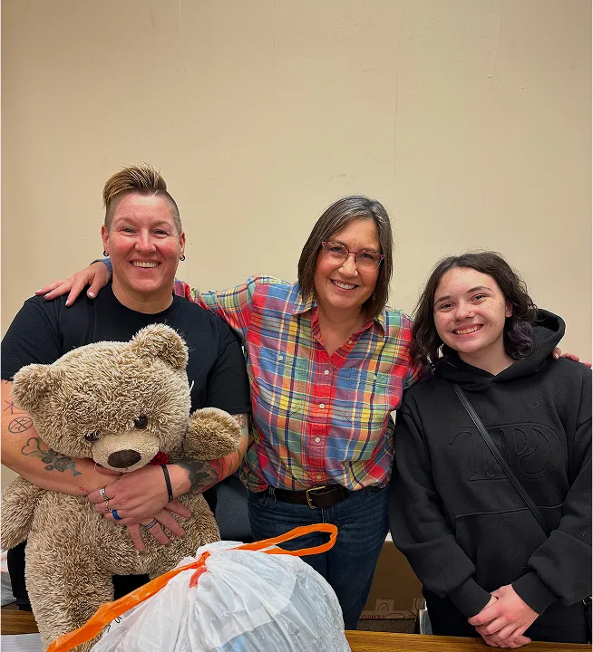 Group of friends smiling with a teddy bear and donation bag at Switch Society community event.