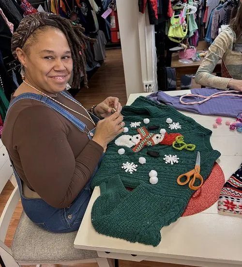 Smiling woman adding decorations to a green Christmas sweater during Switch Society upcycling workshop.