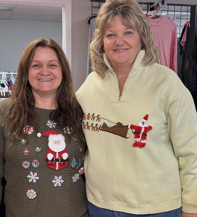 Two women smiling in festive Christmas sweaters at Switch Society sustainable fashion event.
