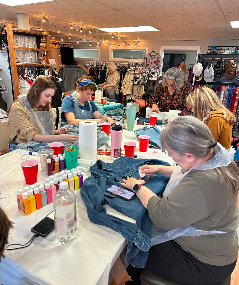 Group of women upcycling denim clothing with paint and sewing during a Switch Society sustainable fashion workshop.
