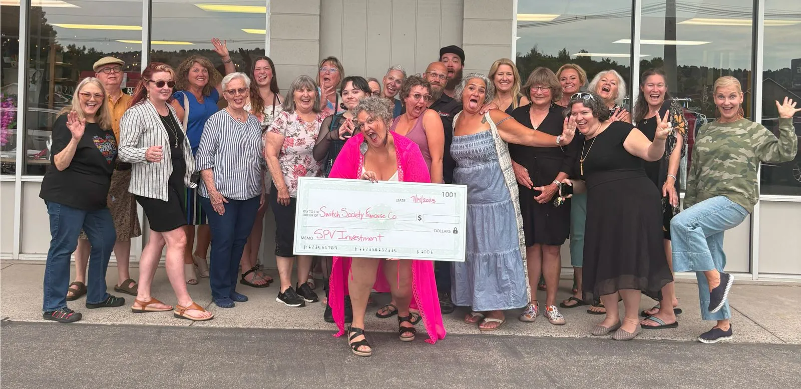 Switch Society community celebrating outside thrift store with a large donation check for sustainable fashion franchise growth.