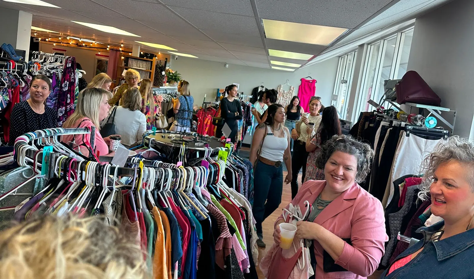 Customers browsing racks of secondhand clothes and chatting during a busy day at Switch Society thrift store.