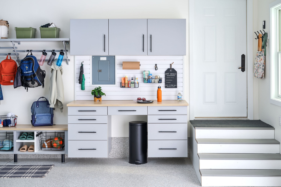 Organized home garage with built-in cabinets, wall-mounted storage, shelving, backpacks, shoes, and household supplies.