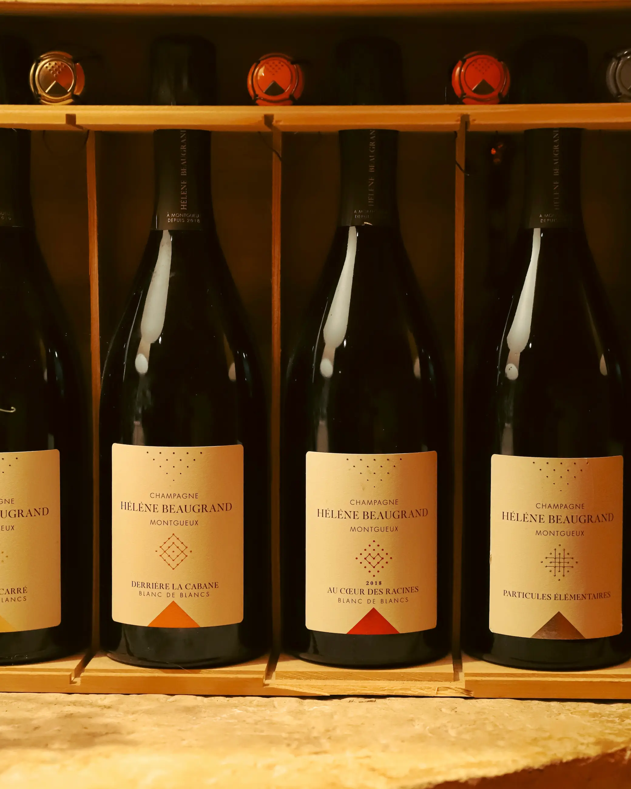 A close-up view of four bottles of Champagne from Hélène Beaugrand, neatly displayed in a wooden rack, each with elegant minimalist labels showcasing different cuvées from Montgueux
