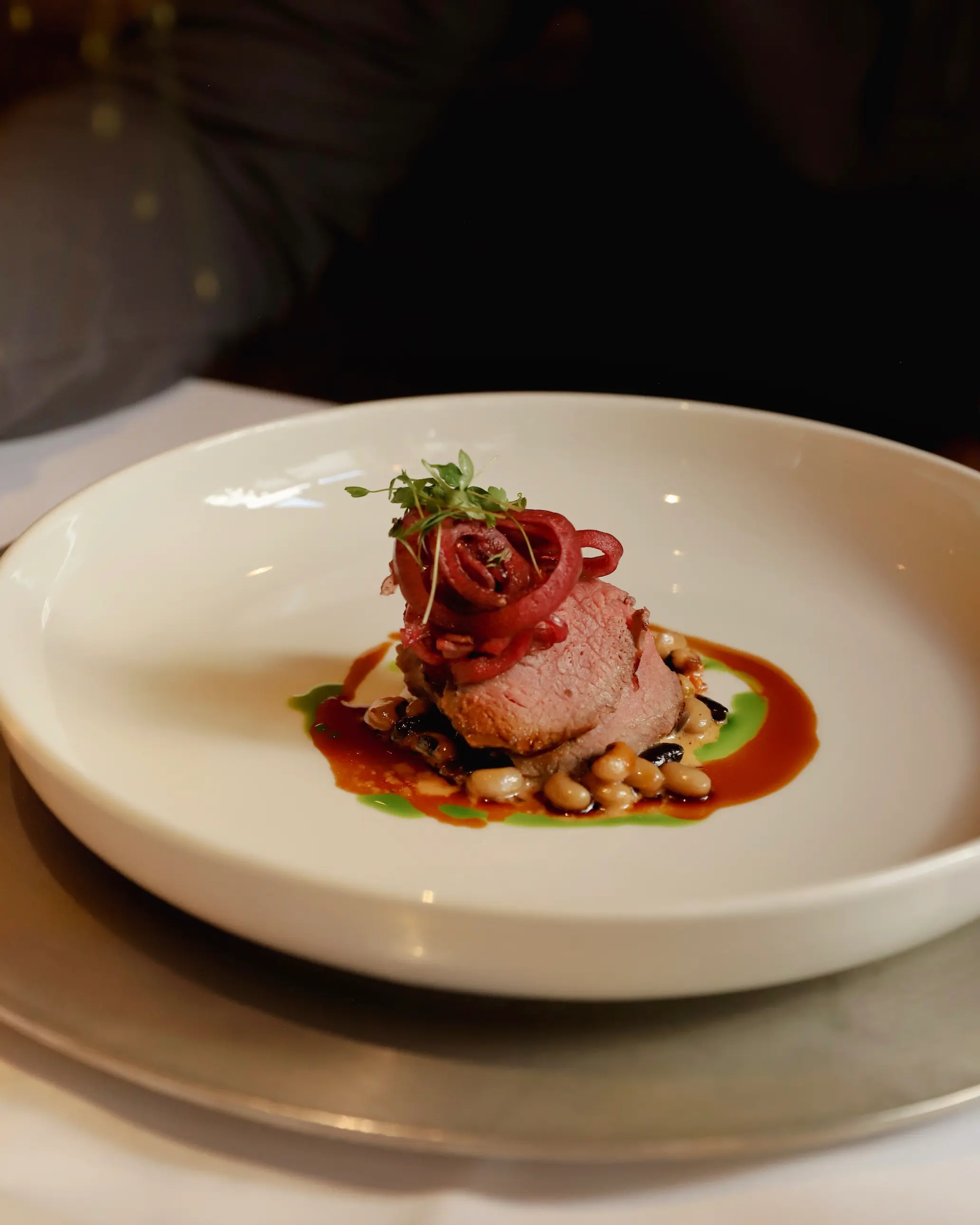 Plated dish of whole-grilled saddle of beef at Schlosshotel Fiss, served with a medley of beans, pickled red onion, microgreens, and tarragon jus.