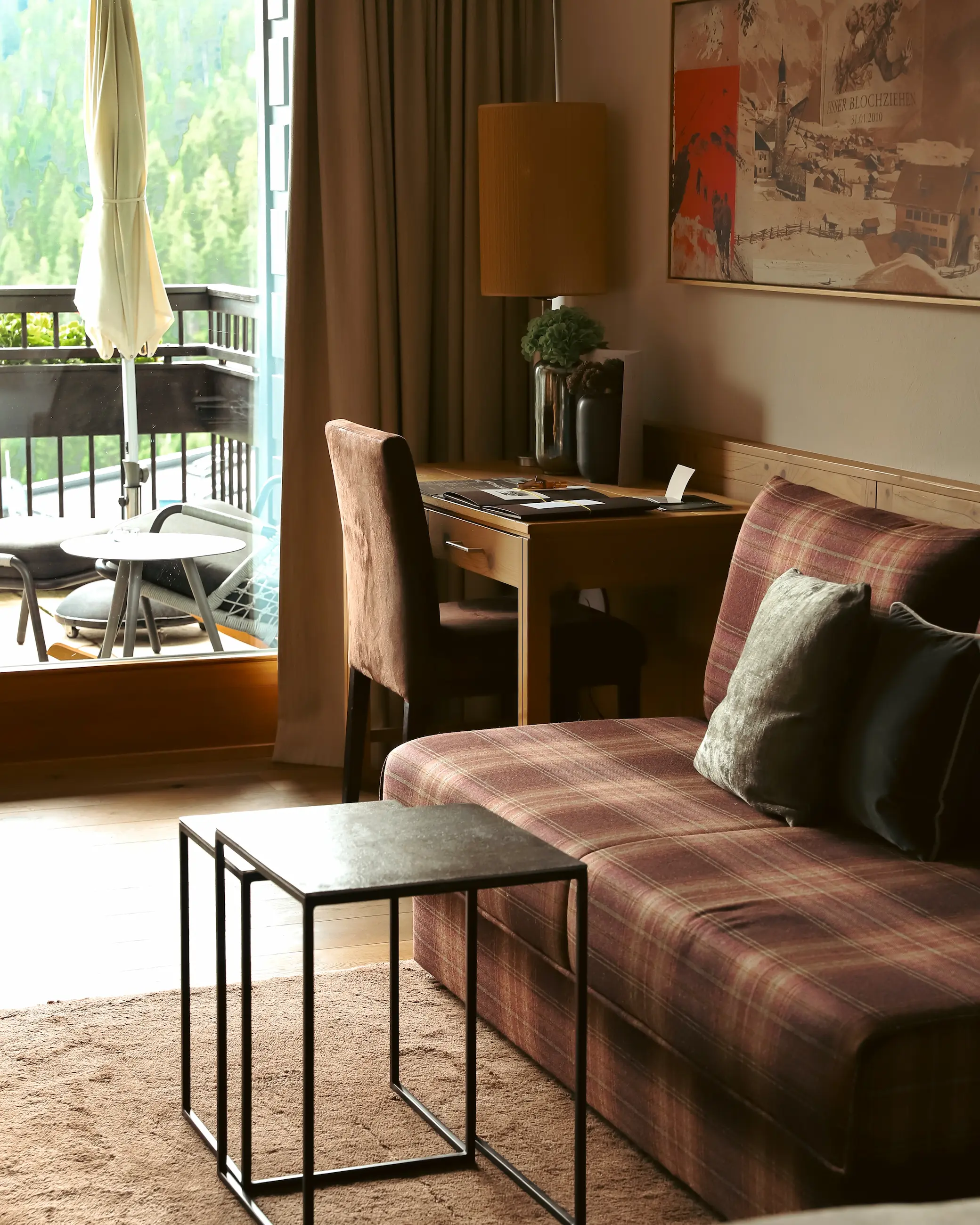 Cosy alpine-style hotel suite at Schlosshotel Fiss featuring a tartan sofa, wooden desk, and balcony with mountain views