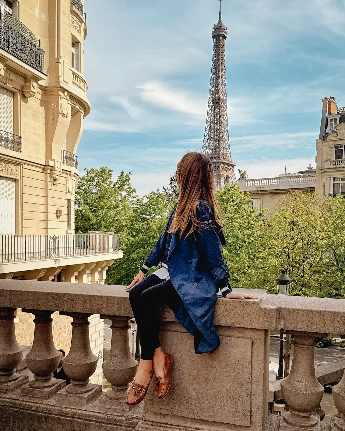 Woman overlooking the Eiffel Tower from Avenue de Camoens in Paris with classic Haussmann architecture on a sunny spring day.