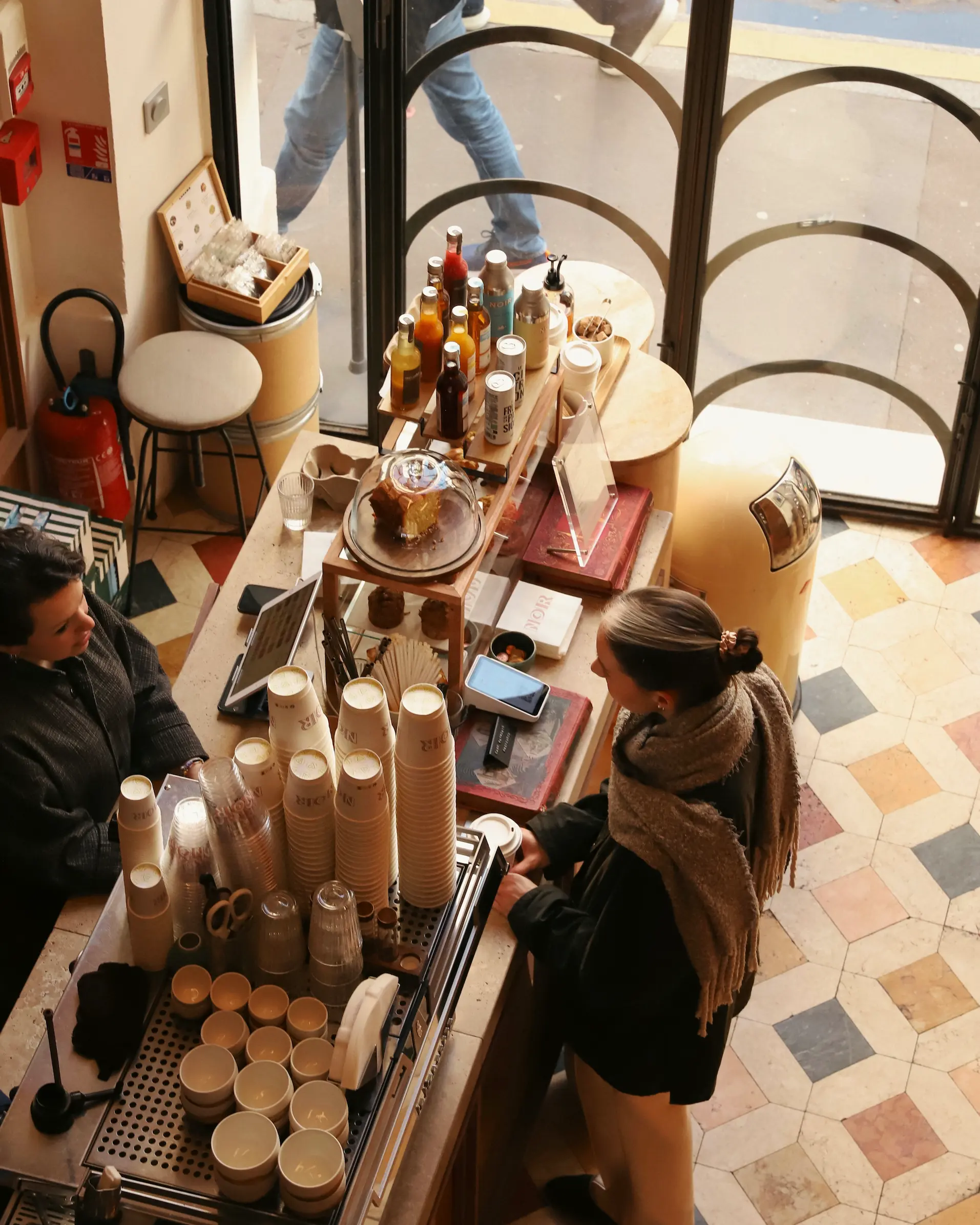 Overhead view inside Café Noir Paris showing barista counter, coffee cups and customers in a cosy Paris coffee shop.