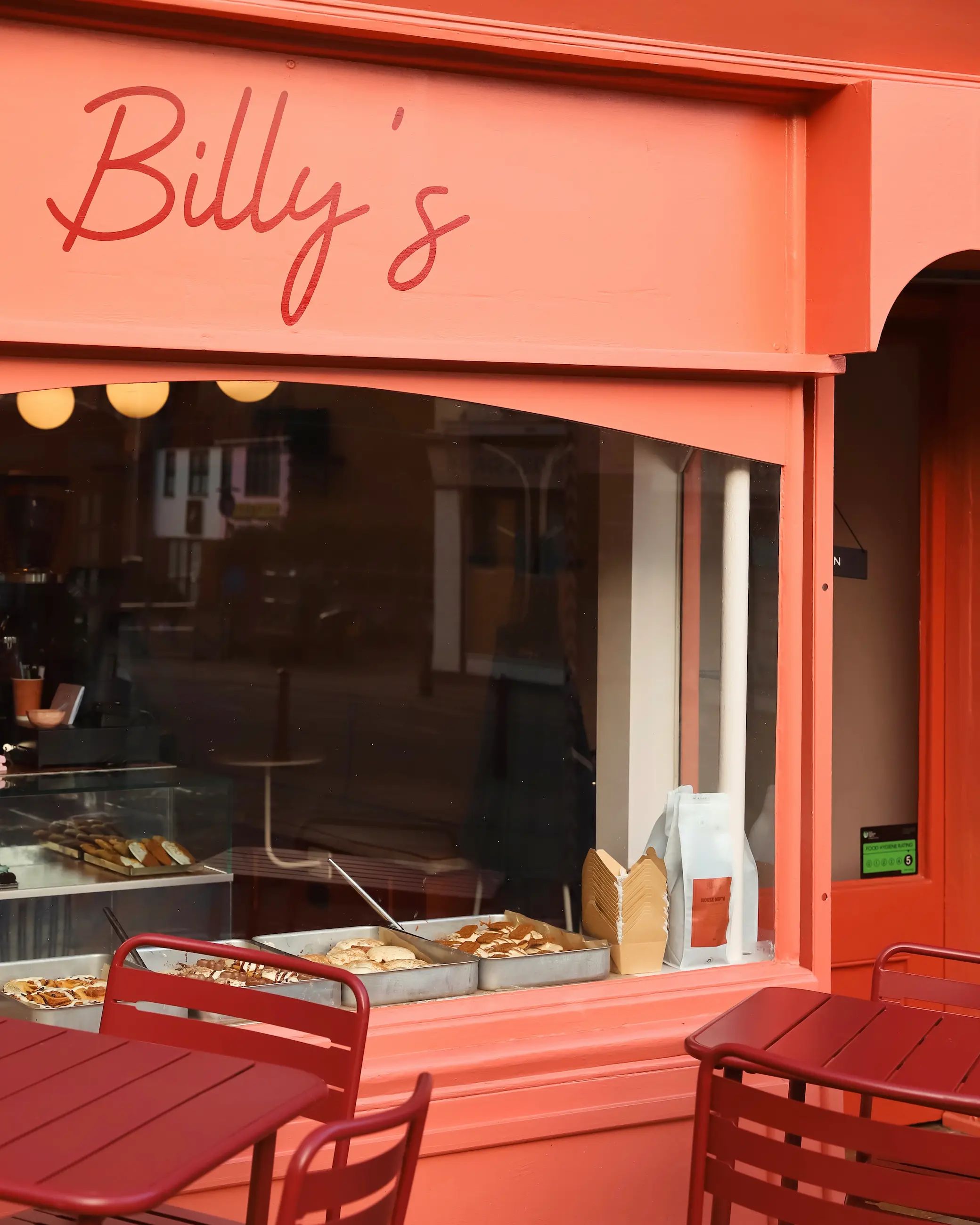 Exterior of Billy’s café in Norwich, with its bright coral storefront, window display of pastries and outdoor seating.