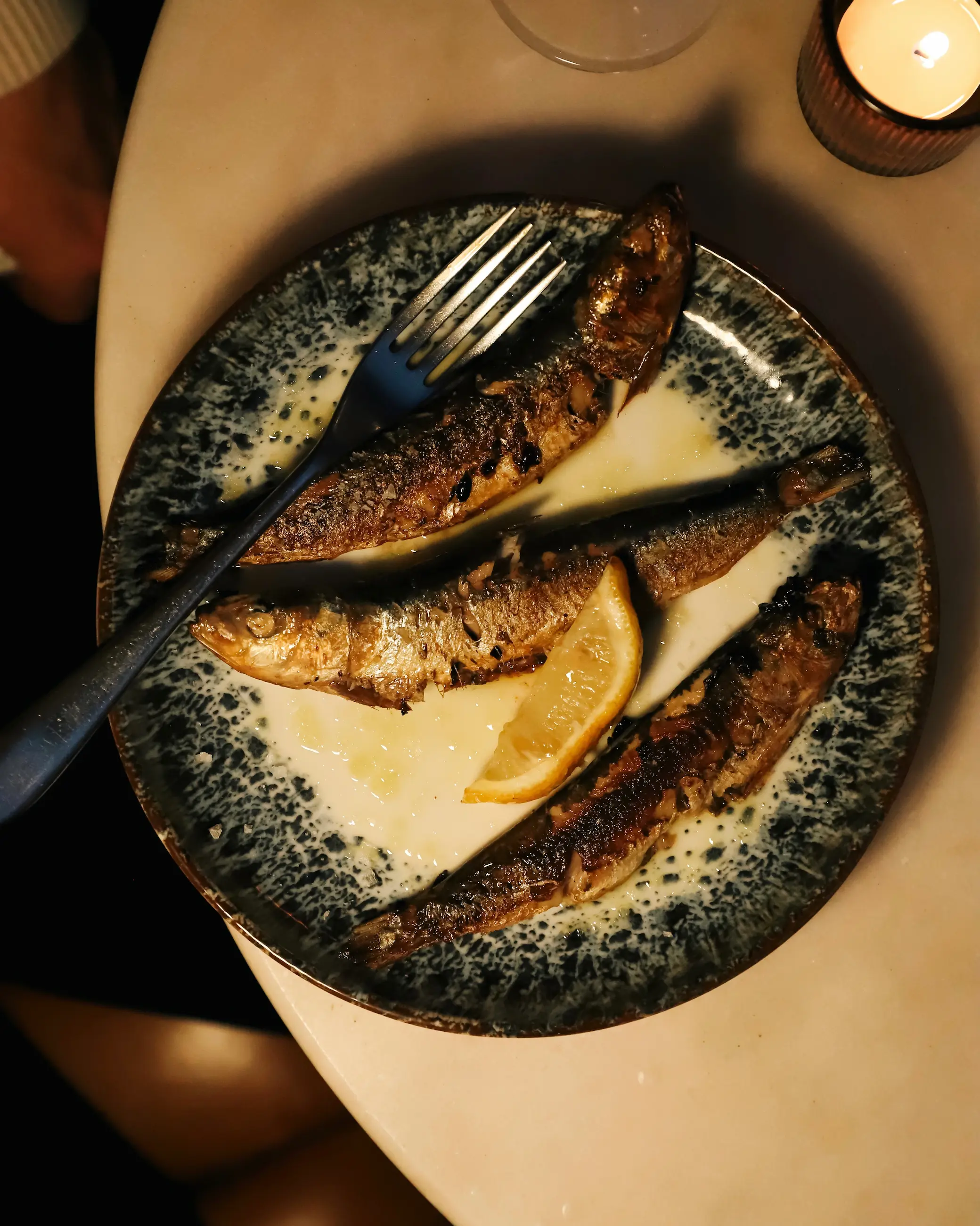 Grilled sardines served with lemon on a plate at Melville’s restaurant in Norwich, lit by candlelight.