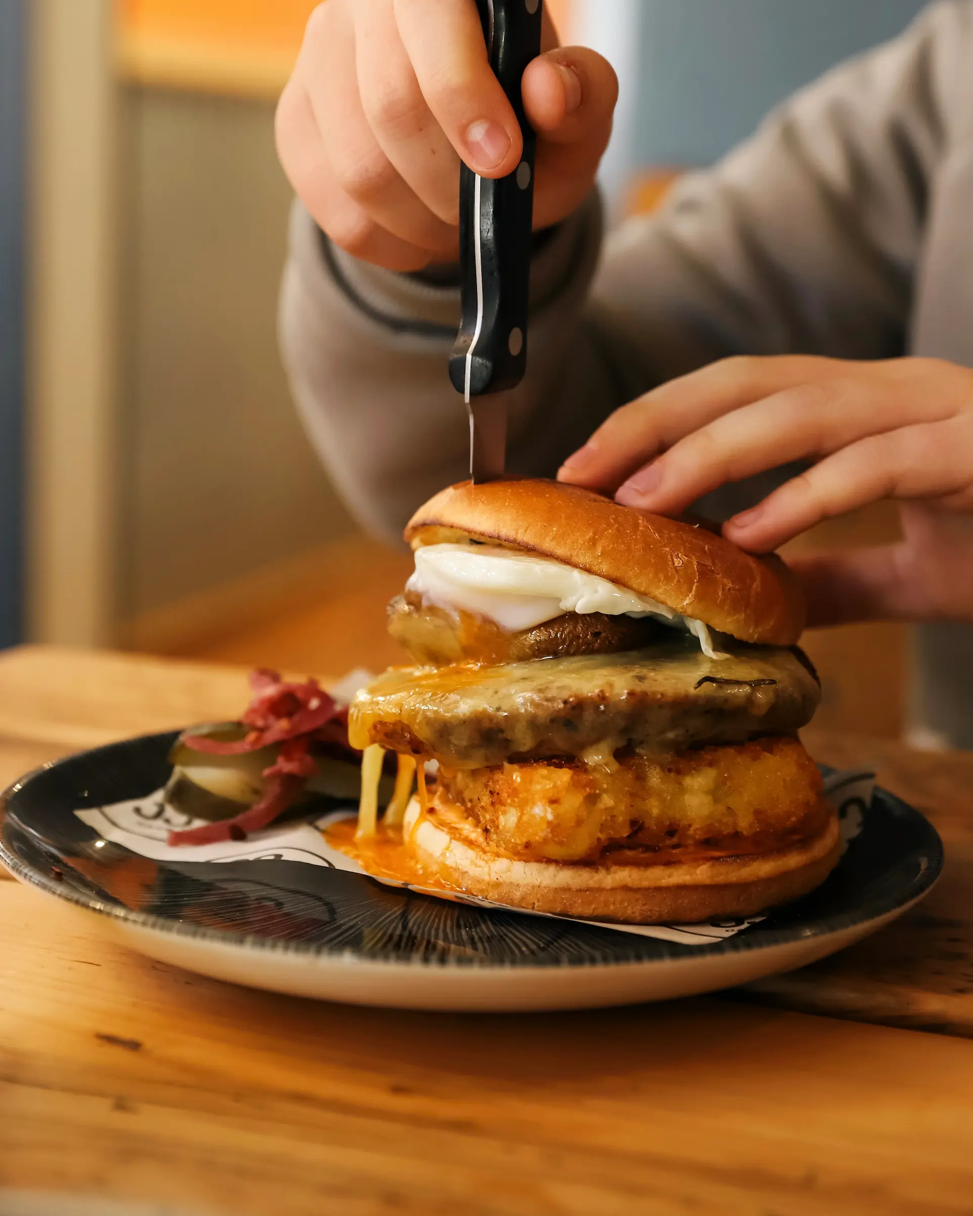 Brunch burger with melted cheese and fried egg being cut on a plate at Café No.33 in Norwich.