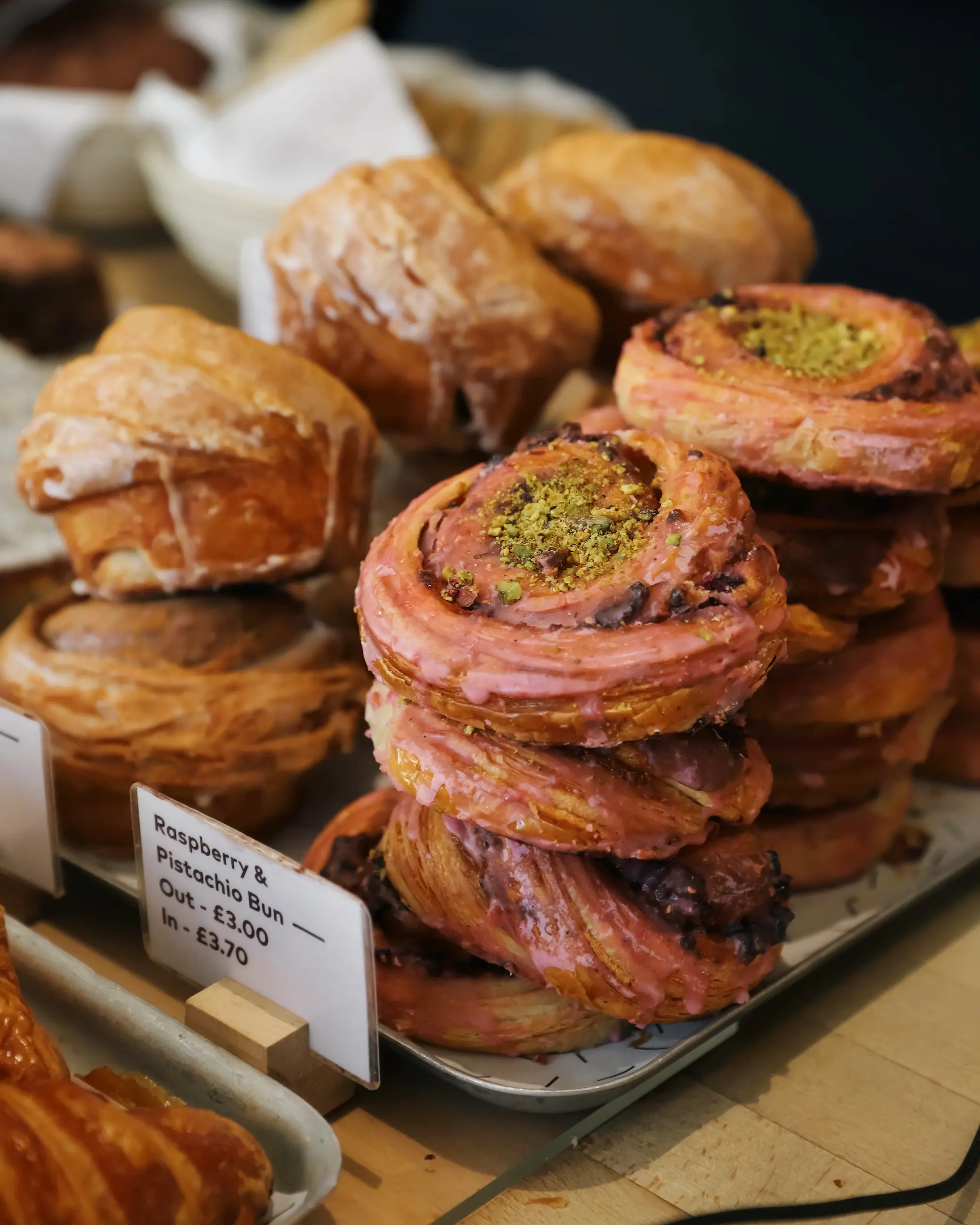 Pastries on display at Bread Source bakery in Norwich, including raspberry and pistachio buns and glazed pastries.