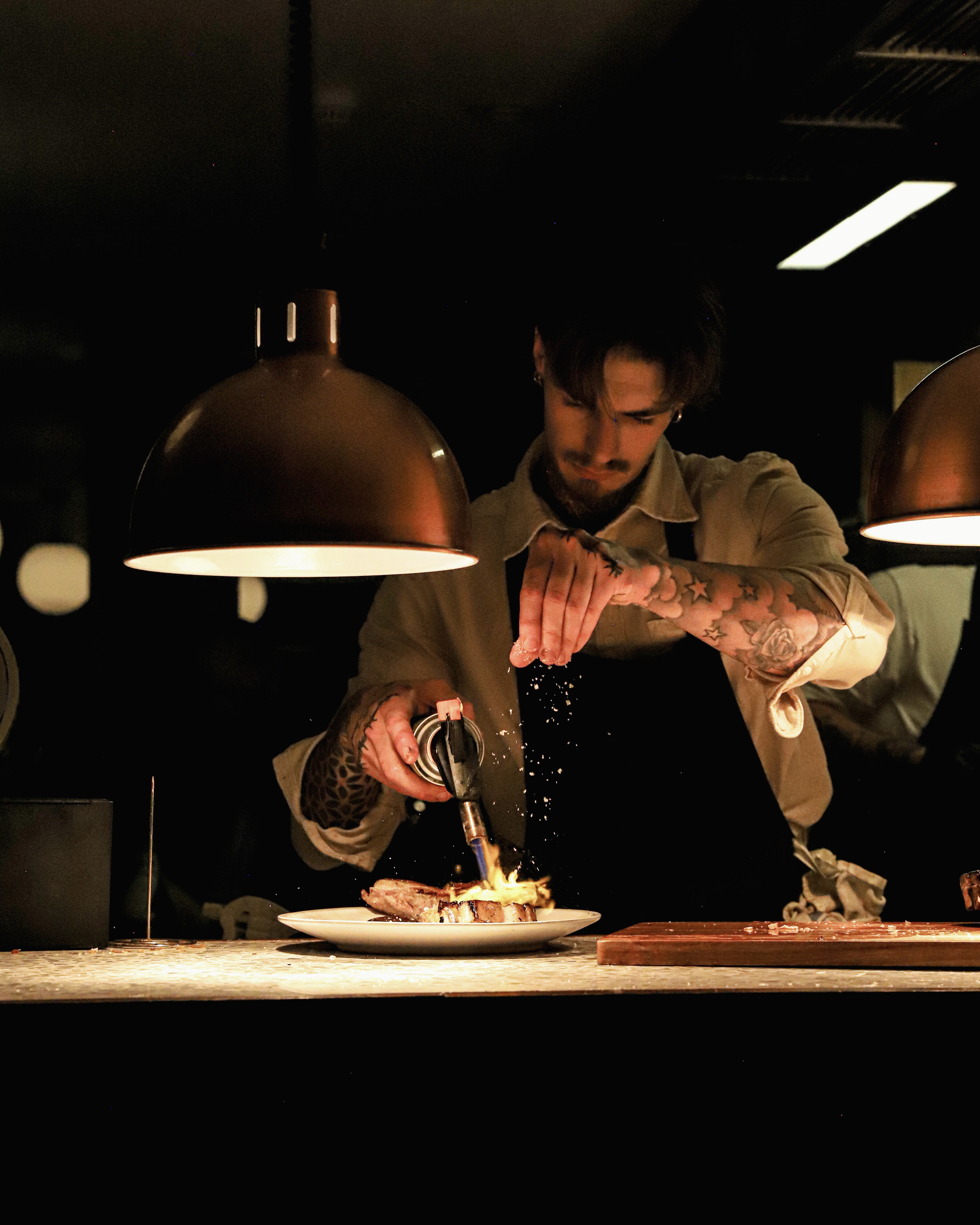 Chef finishing a dish with a blowtorch in a dimly lit restaurant kitchen at Melville’s in Norwich.